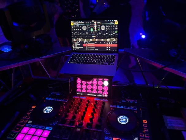DJ-Setup mit Laptop und Mischpult, umgeben von bunten Lichtern.