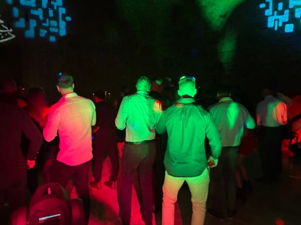 Menschen in formeller Kleidung stehen in einem beleuchteten Raum mit grünem und rotem Licht.