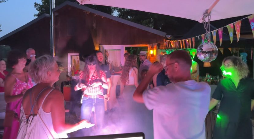 Menschen feiern mit Lichtern und Rauch auf einer lebhaften Sommerparty im Freien.