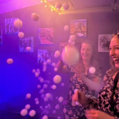 Zwei Frauen lachen und werfen Bälle in einer bunten, beleuchteten Umgebung.