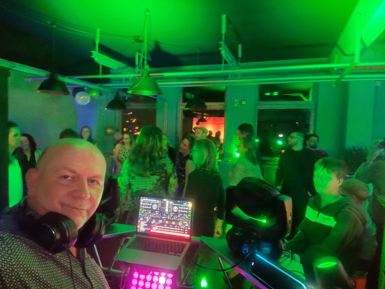 DJ mit Kopfhörern vor einer tanzenden Menge in einem beleuchteten Club.