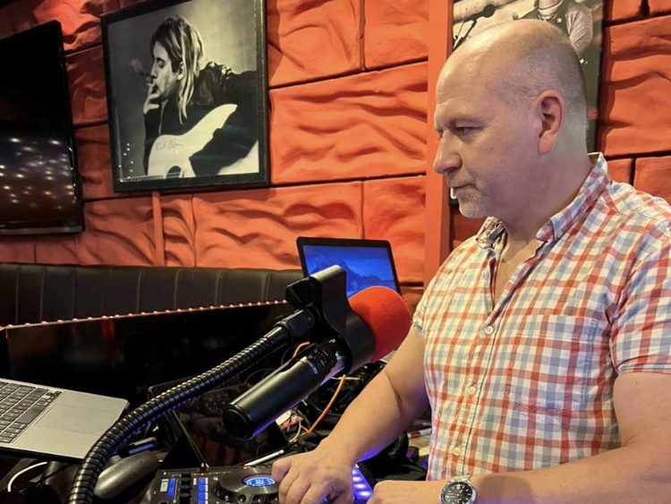 DJ MP 1 für Berlin & Brandenburg Mann bedient DJ-Equipment in einer Bar mit rotem Hintergrund.