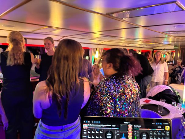 Firmen-Event auf der Spree in Berlin - Treptow - Mitte - Tiergarten Eine lebhafte Party mit mehreren Personen auf einer Tanzfläche. DJ-Pult im Vordergrund.