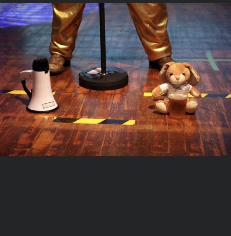 Ein Mikrofonständer, ein Megaphon und ein Teddybär auf einem Holzboden.