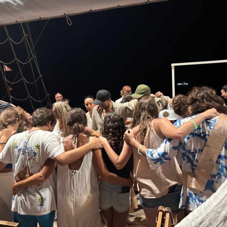 Gruppe von Menschen umarmt sich auf einem Schiff bei Nacht.