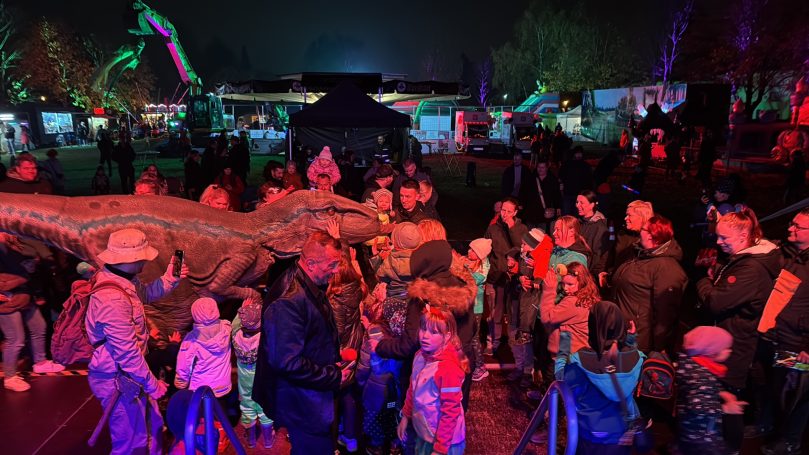 Menschenmenge bei einer nächtlichen Veranstaltung mit bunten Lichtern und Attraktionen.