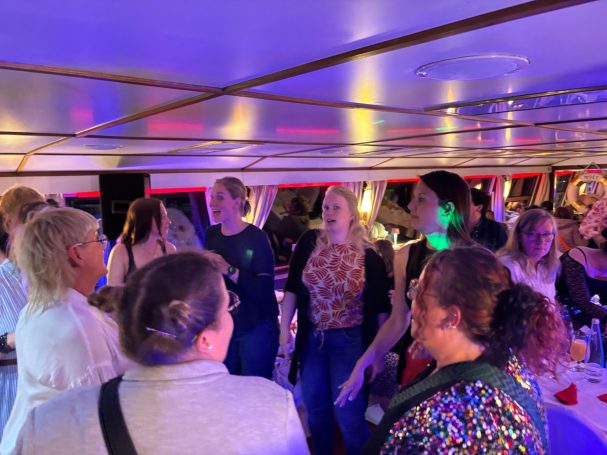 Party auf dem Party- & Event-Schiff, MS Diva Gruppe von Menschen feiert auf einem Boot mit bunten Lichtern und fröhlicher Stimmung.