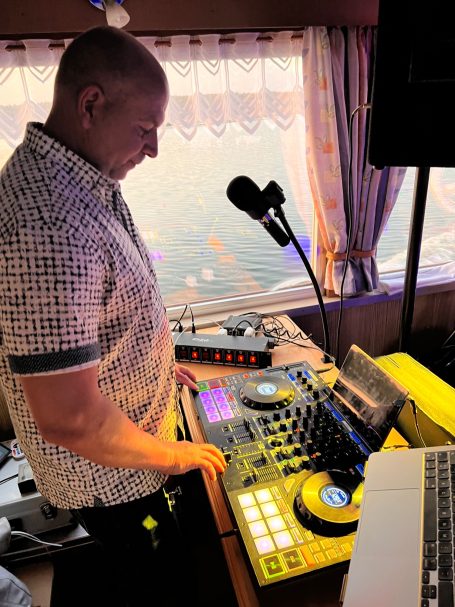 DJ steht an einem Mischpult mit farbigen Lichtern in einer Innenraumszene.