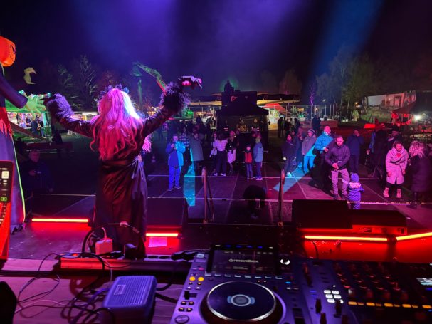 DJ in Schwarz mit erhobenen Armen vor tanzender Menge bei nächtlichem Festival.