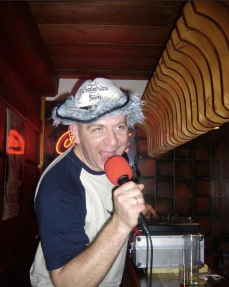 Mann mit Mikrofon und ausgefallenem Hut singt in einer Bar.