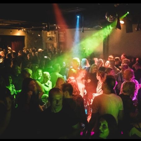 Menschen tanzen in einem Club mit bunten Lichtern und einer lebhaften Atmosphäre.